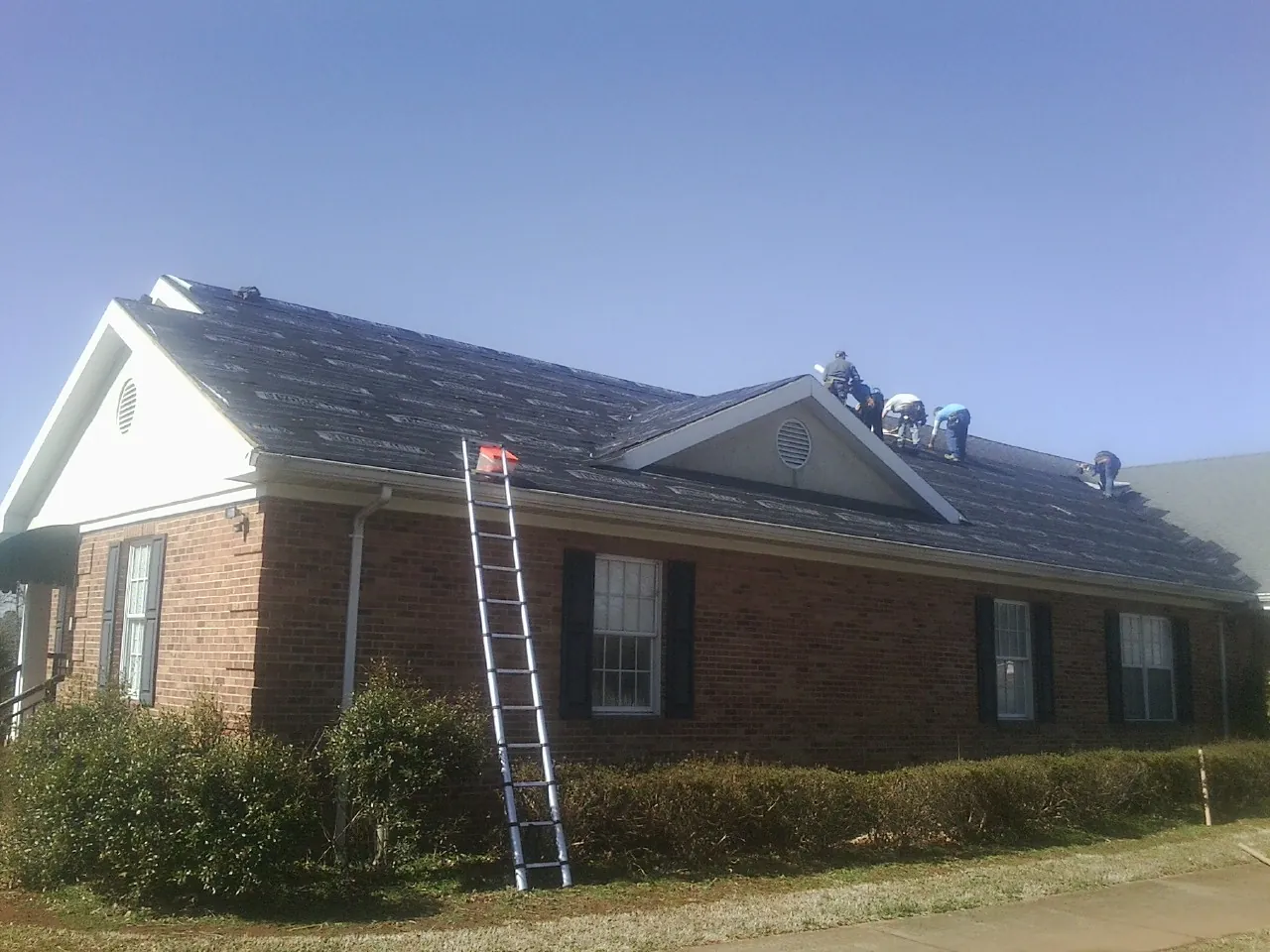 Crew tearing shingles off a brick ranch roof with a ladder set — Emergency Roof Repair work by our crew in Savannah